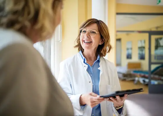 Shot of a smiling senior doctor with a digital tablet talking to a female patient at hospital. Medical professional discussing with woman at nursing home.